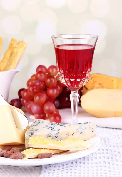 Placa de queso surtido, copa de uva y vino en la mesa, sobre fondo claro —  Fotos de Stock