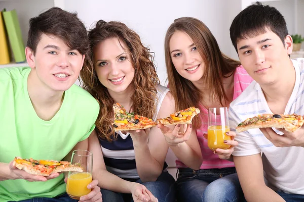 Skupina mladých přátel, jíst pizzu v obýváku na pohovce — Stock fotografie