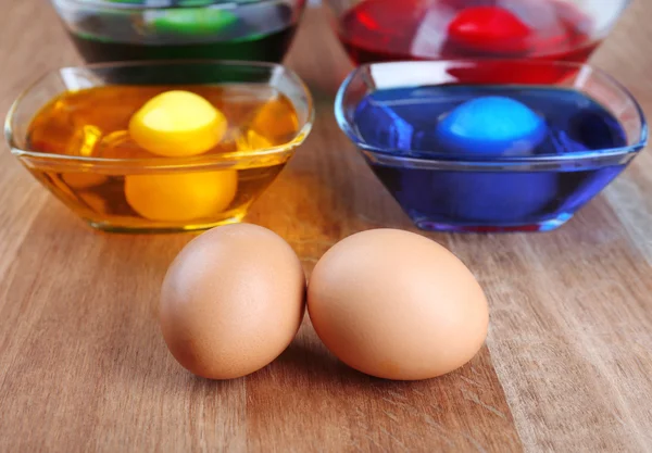 Tigelas com tinta para ovos de Páscoa e ovos em mesa de madeira — Fotografia de Stock