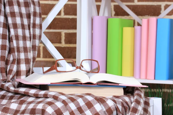 Samenstelling met glazen en boeken, op stoel, op kabinet en muur achtergrond — Stockfoto