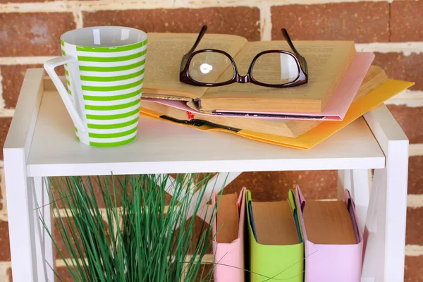 Composição com óculos e livros, no armário, no fundo da parede de cor — Fotografia de Stock