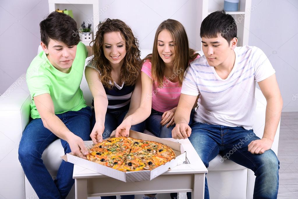 Group of young friends eating pizza in living-room on sofa