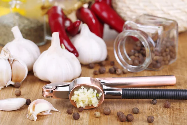 Samenstelling met knoflook press, verse knoflook en glazen potten met specerijen op houten achtergrond — Stockfoto