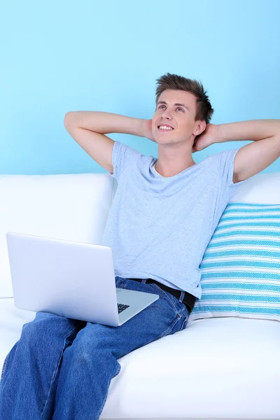 Guy sitting on sofa with laptop on blue background — Stock Photo, Image