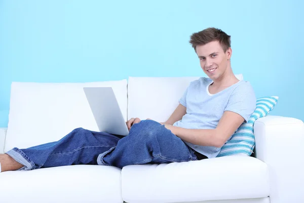 Cara mentira no sofá com laptop no fundo azul — Fotografia de Stock