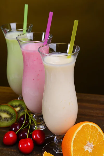 Milk shakes with fruits on table on dark yellow background — Stock Photo, Image