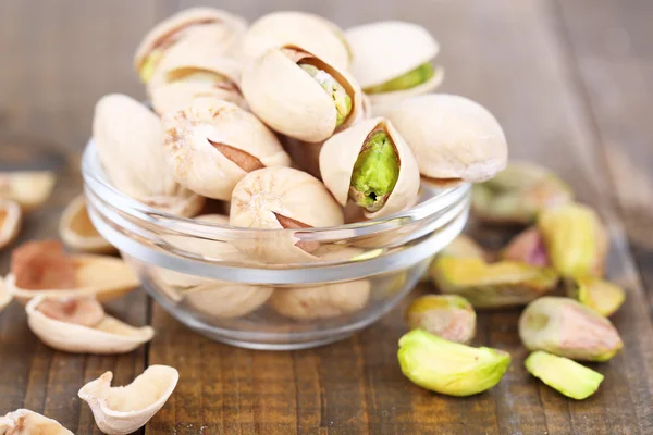 Nueces de pistacho en cuenco de vidrio sobre fondo de madera — Foto de Stock