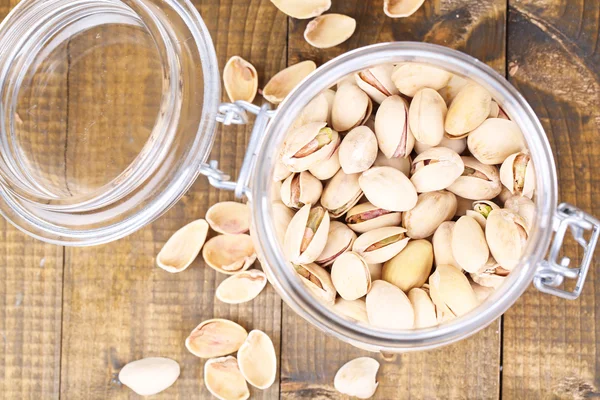 Pistachio nuts in glass jar on wooden background — Stock Photo, Image