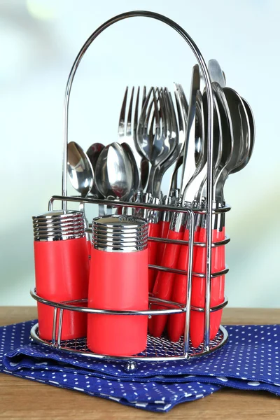 Kitchen cutlery in metal stand on wooden table on bright background — Stock Photo, Image