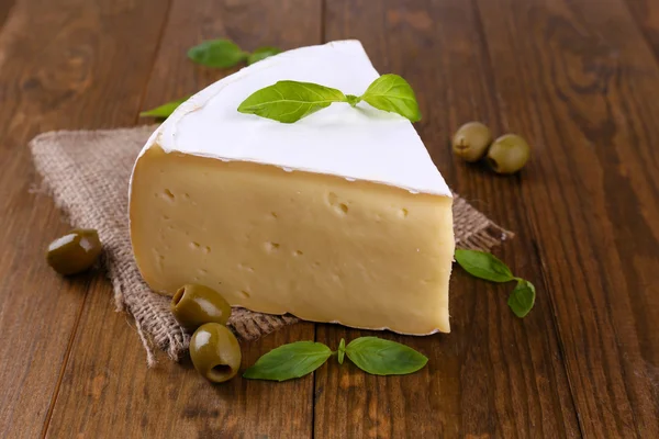 Queijo saboroso Camembert com manjericão e azeitonas, sobre mesa de madeira — Fotografia de Stock