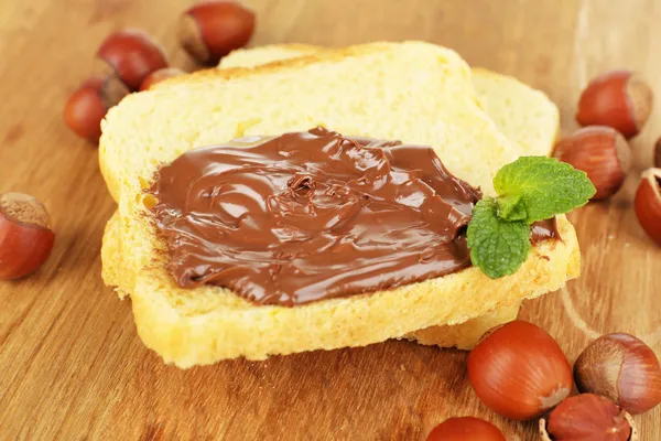 Roti dengan coklat manis hazelnut menyebar di latar belakang kayu — Stok Foto