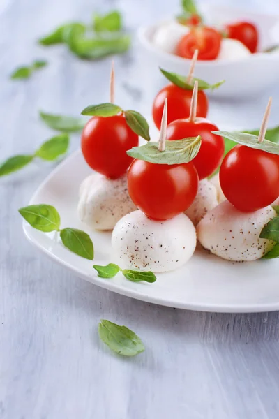 Smakelijke mozzarella kaas met basilicum en tomaten op plaat, op houten tafel — Stockfoto