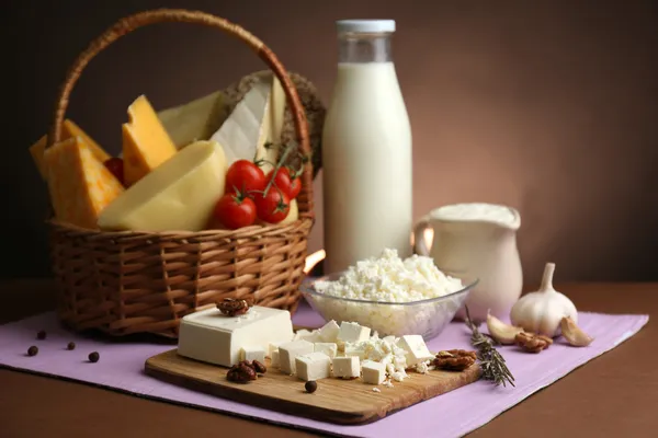 Cesta com produtos lácteos saborosos na mesa de madeira, no fundo marrom escuro — Fotografia de Stock
