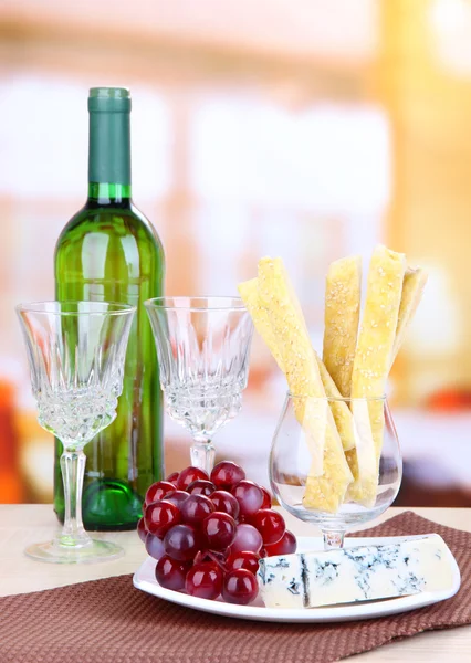明るい背景上の木製テーブル上プレート上にチーズ、ブドウ、パン棒 — ストック写真
