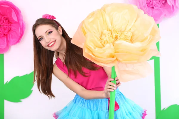 Hermosa mujer joven en falda pequeña sosteniendo gran flor sobre fondo decorativo —  Fotos de Stock