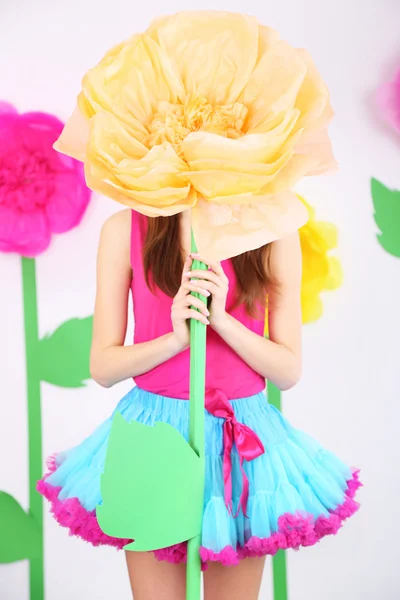 Schöne junge Frau im kleinen Rock hält große Blume auf dekorativem Hintergrund — Stockfoto