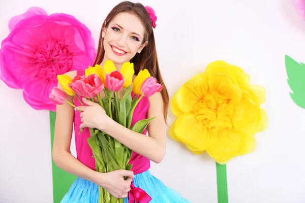 Schöne junge Frau mit einem Strauß Tulpen auf dekorativem Hintergrund — Stockfoto