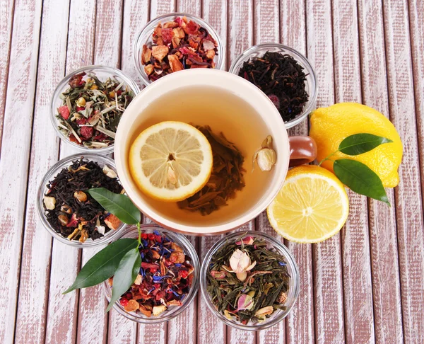 Tasse Tee mit aromatischem, trockenem Tee in Schalen auf Holzgrund — Stockfoto