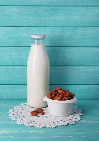 Мигдальне молоко в пляшці з мигдалем в мисці, на кольоровому дерев'яному фоні — стокове фото
