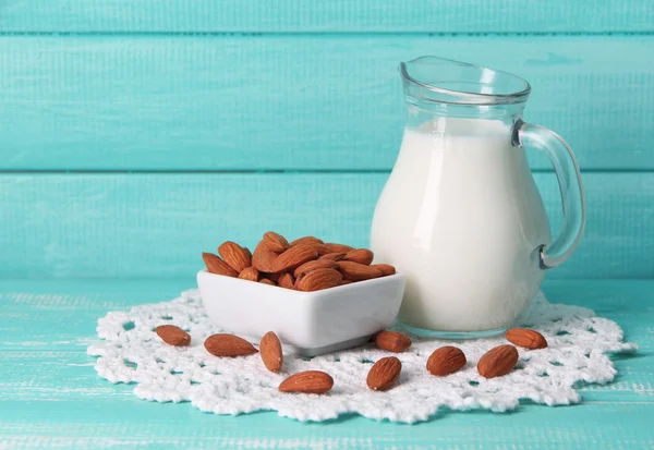 Almond milk in jug with almonds in bowl, on color wooden background — Stock Photo, Image