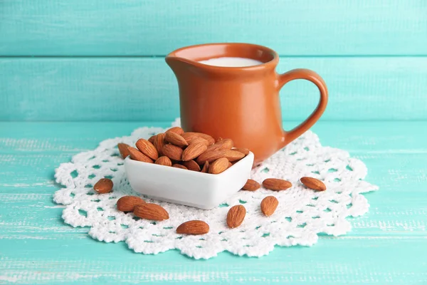 Almond milk in jug with almonds in bowl, on color wooden background — Stock Photo, Image