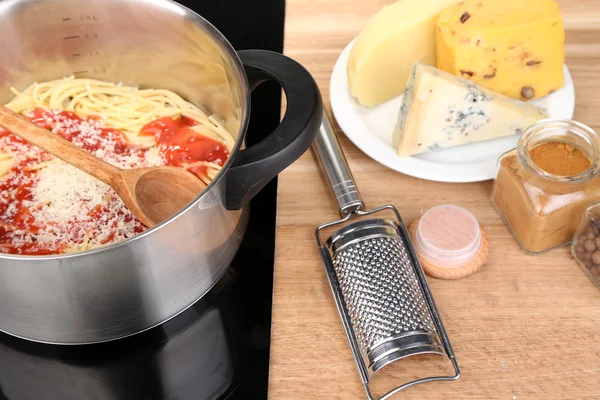 Composition with tasty spaghetti in pan, grater, cheese, on wooden table background — Stock Photo, Image