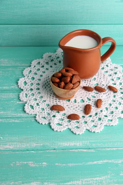 Almond milk in jug with almonds in bowl, on color wooden background — Stock Photo, Image