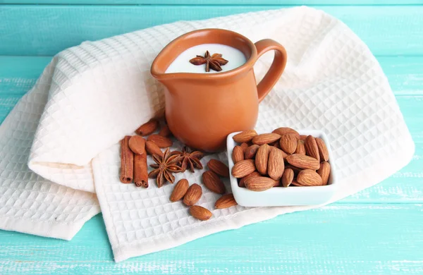 Almond milk in jug with almonds in bowl, on color wooden background — Stock Photo, Image