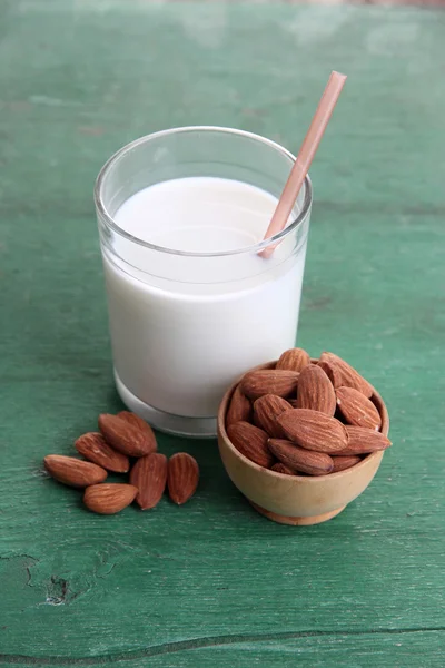 Latte di mandorle in vetro con mandorle in ciotola, su sfondo di legno a colori — Foto Stock