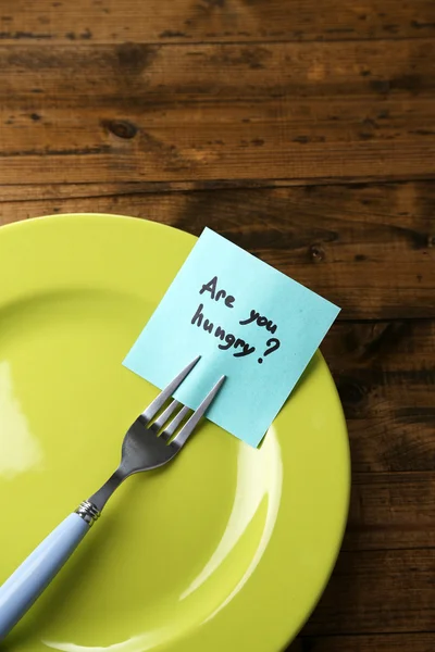 Note paper with message  attached to fork, on plate, on wooden background — Stock Photo, Image