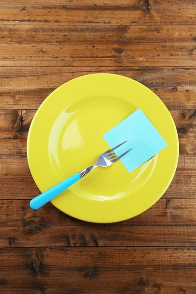 Empty note paper attached to fork, on plate, on color wooden background — Stock Photo, Image