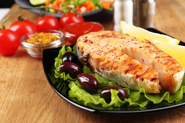 Salmão grelhado saboroso com limão e legumes, na mesa de madeira — Fotografia de Stock