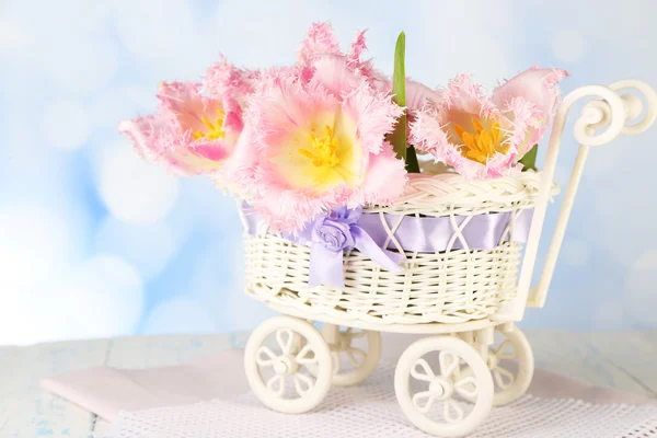 Beautiful tulips in decorative wicker basket, on wooden table, on light background — Stock Photo, Image