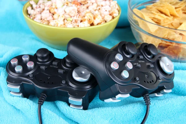 Controladores de juego negro y tazón con bocadillos sobre fondo a cuadros de color —  Fotos de Stock