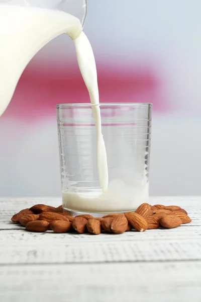 Мигдальне молоко насипають у склянку, на кольоровий дерев'яний стіл, на світлому фоні — стокове фото