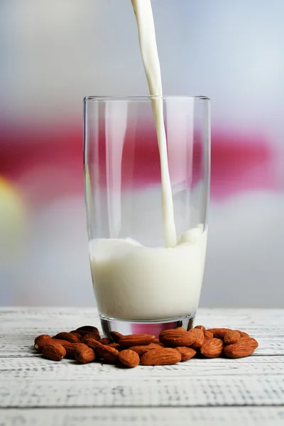 Mandelmilch wird in Glas gegossen, auf farbigem Holztisch, auf hellem Hintergrund — Stockfoto