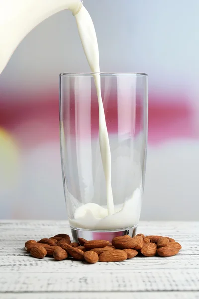 Il latte di mandorla viene versato nel vetro, sul tavolo di legno a colori, su sfondo chiaro — Foto Stock