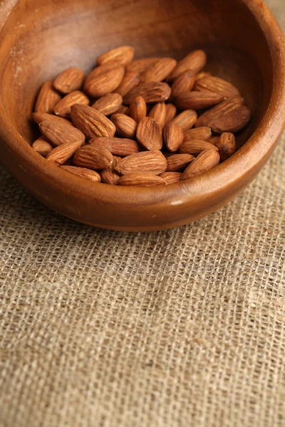 Almonds in bowl on sackcloth background — Stock Photo, Image