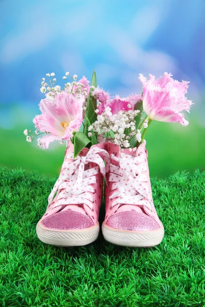 Hermosos zapatos de goma con flores en el interior sobre hierba verde, sobre fondo brillante — Foto de Stock