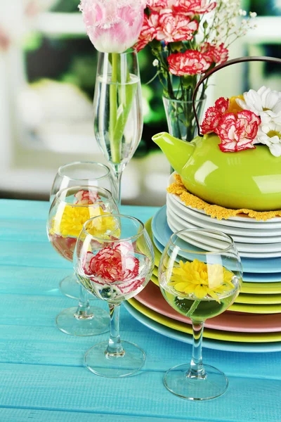 Stack of colorful ceramic dishes and flowers, on wooden table, on light background — Stock Photo, Image