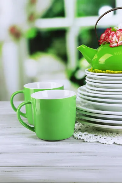 Stapel von bunten Keramikgeschirr und Blumen, auf Holztisch, auf hellem Hintergrund — Stockfoto