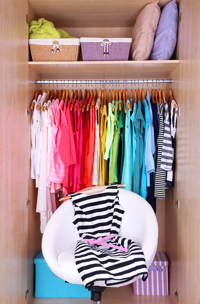 Female clothes in wardrobe and chair in room — Stock Photo, Image