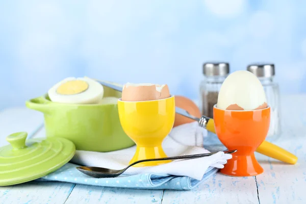 Huevos cocidos en sartén y taza de huevo sobre mesa de madera de color, sobre fondo claro —  Fotos de Stock