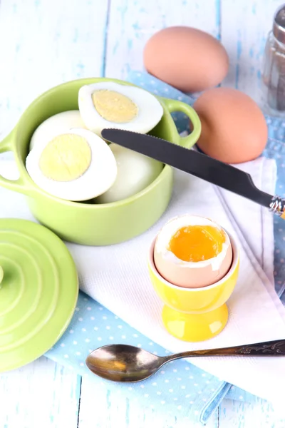 Boiled eggs in pan and eggcup on color wooden background — Stock Photo, Image