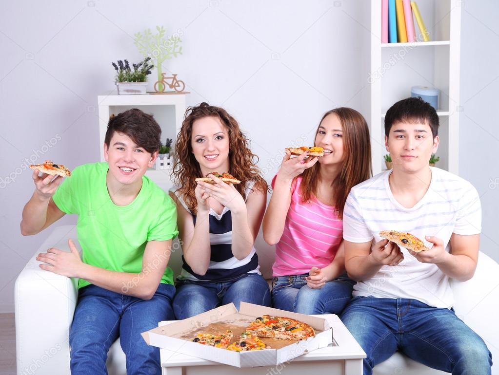 Group of young friends eating pizza in living-room on sofa