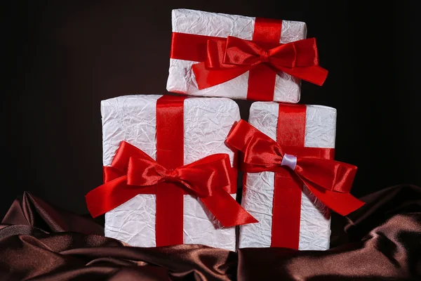 Schöne Geschenke mit roten Bändern auf Seide, auf dunklem Hintergrund — Stockfoto