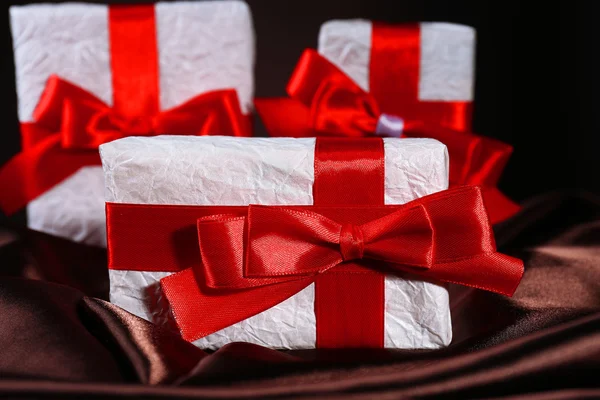 Hermosos regalos con cintas rojas sobre seda, sobre fondo oscuro — Foto de Stock