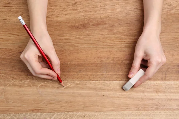 Manos humanas con lápiz y goma de borrar sobre fondo de mesa de madera — Foto de Stock