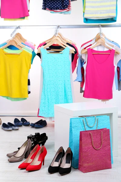 Verschiedene Kleidungsstücke auf Kleiderbügeln und Schuhe auf hellem Hintergrund — Stockfoto