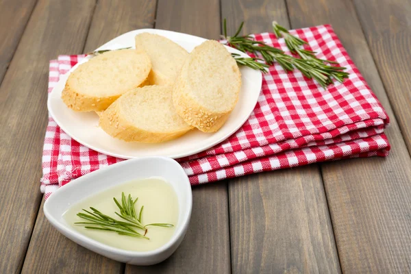 Färskt bröd med olivolja och rosmarin på träbord — Stockfoto